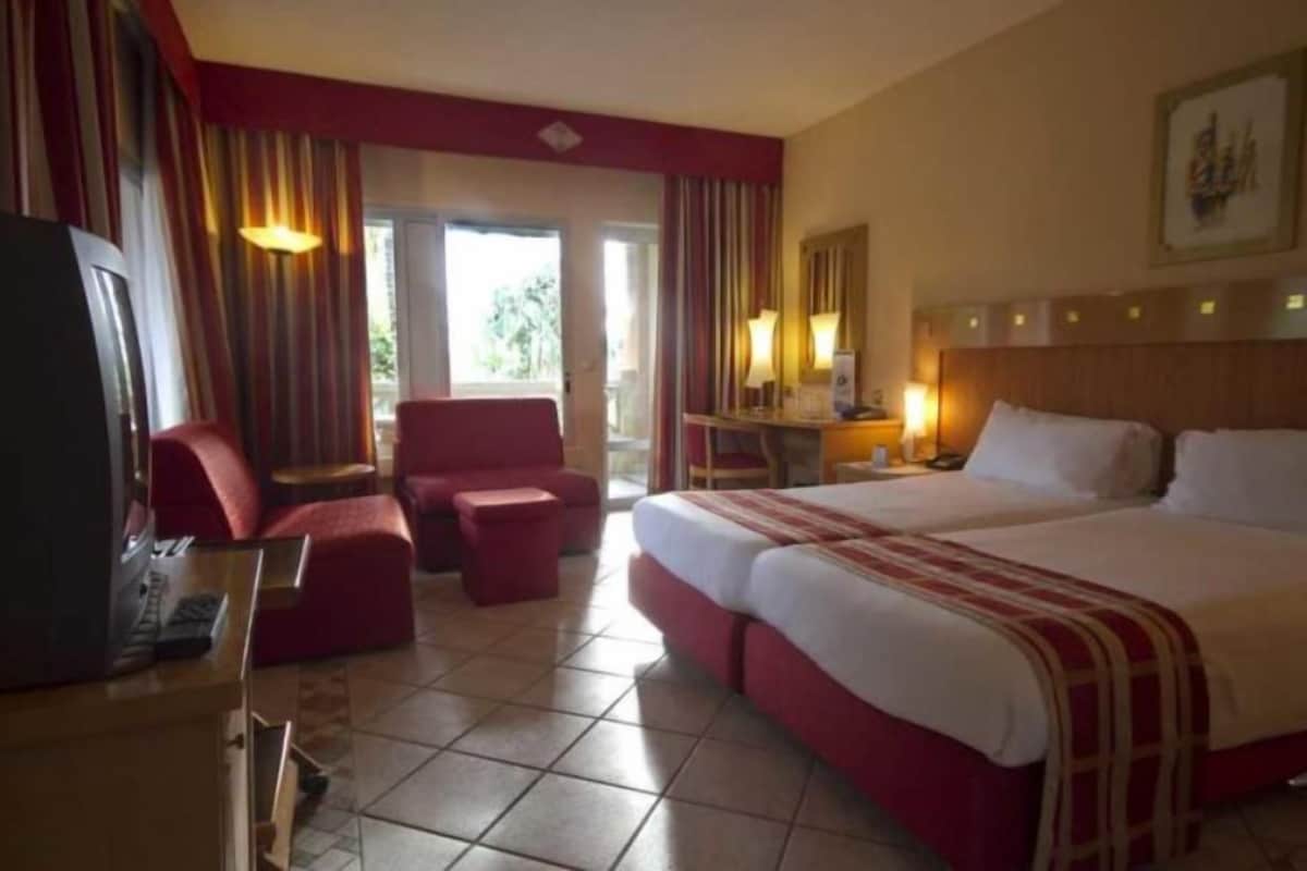 Habitación de hotel con una cama grande, un escritorio con lámpara, una silla y un televisor.