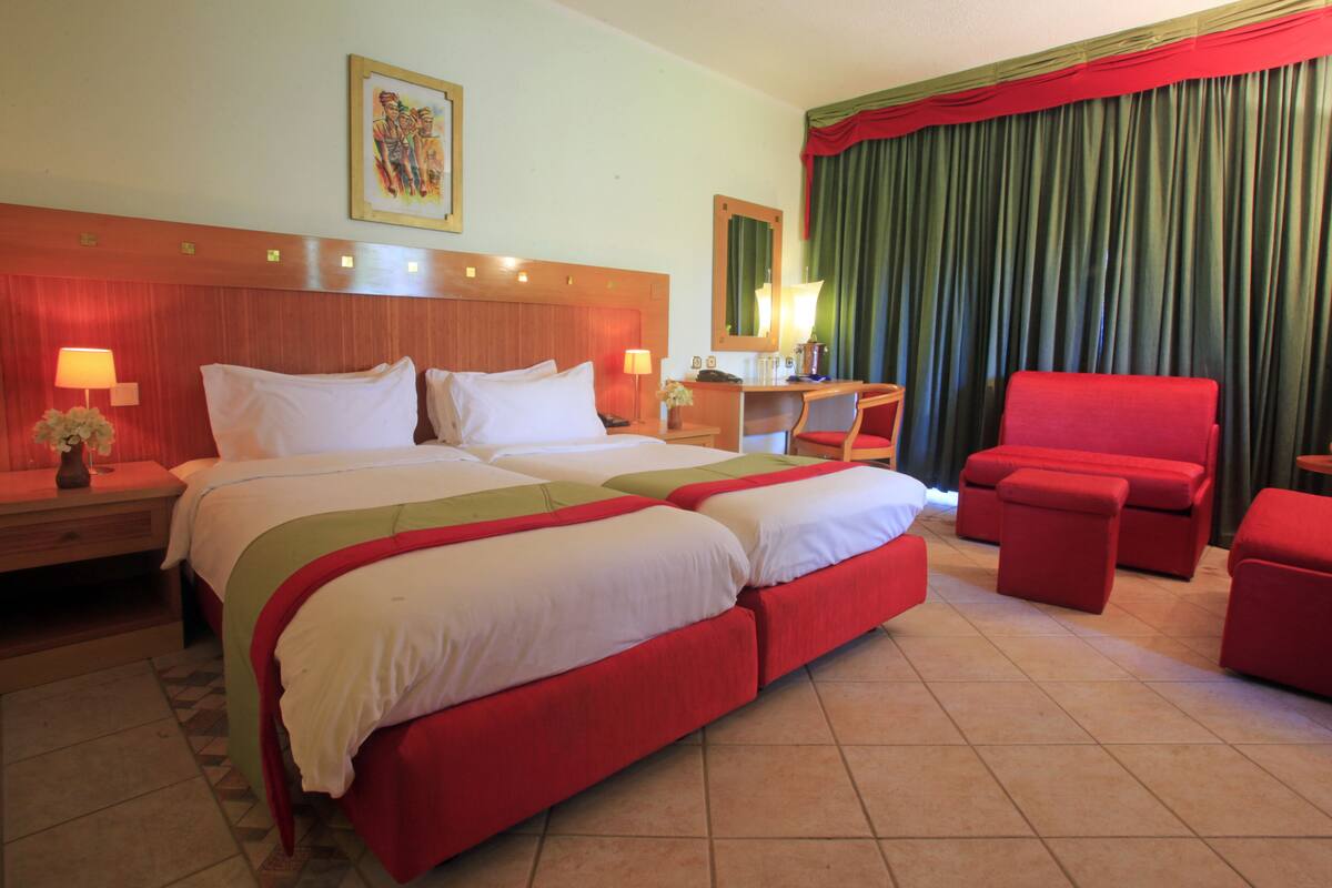 A hotel room with a large bed, two bedside tables, a desk, a chair, and a red armchair.