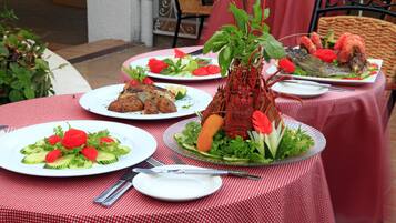 Una mesa dispuesta con platos de comida, incluyendo un langostino, ensalada y otros guisos, sobre un mantel a cuadros rojo y blanco.