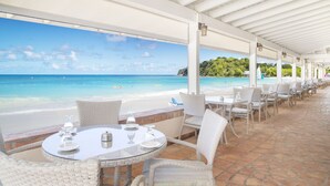 A covered outdoor seating area with tables and chairs overlooking a beach. - Pineapple Beach Club Antigua - Adults Only – All Inclusive (Willikies)