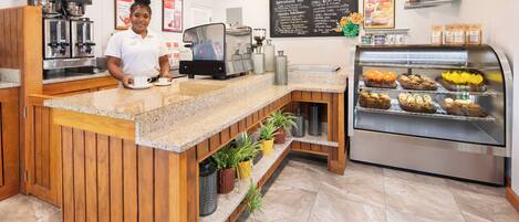A coffee shop interior with a wooden counter, espresso machines, a display case with pastries, and a chalkboard menu.