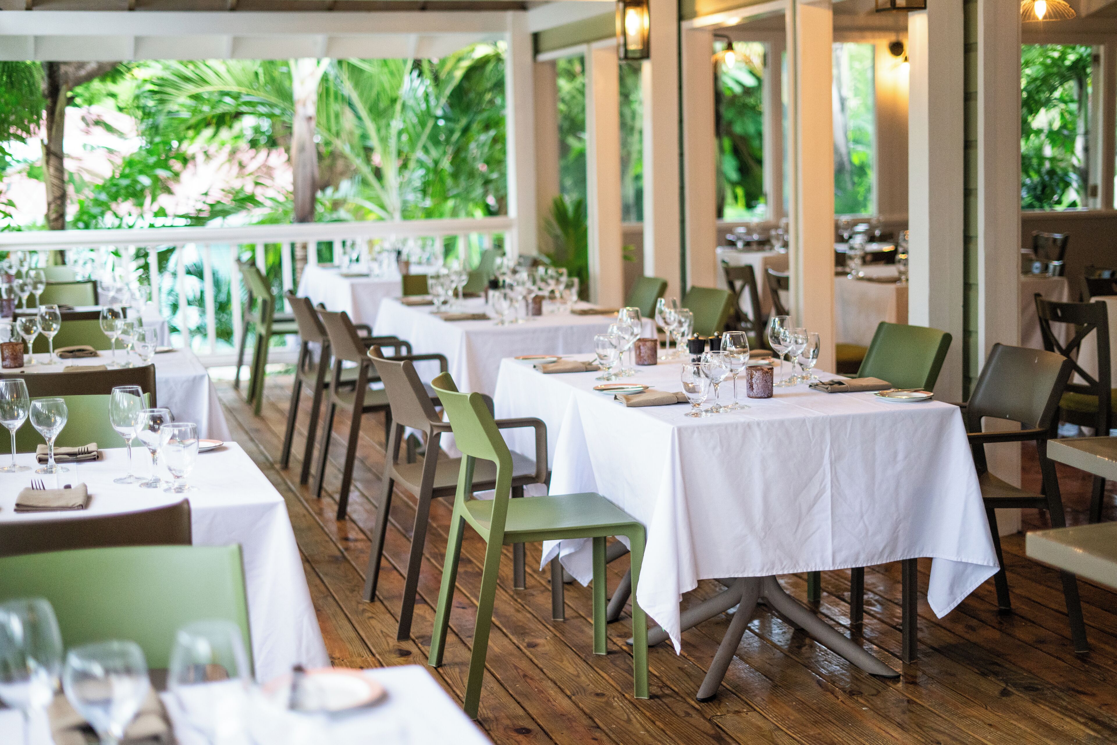A restaurant with multiple tables set for dining, surrounded by greenery.