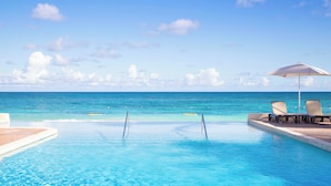 A clear blue pool with a view of the ocean, lounge chairs, and an umbrella. - Pineapple Beach Club Antigua - Adults Only – All Inclusive (Willikies)