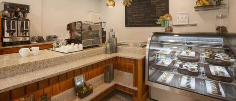 A coffee shop with a counter, espresso machines, a display case with pastries, and a chalkboard menu.