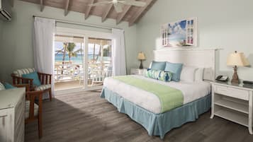 Ein Schlafzimmer mit Bett, Stuhl, Nachttisch und Blick auf den Strand durch eine Schiebetür.