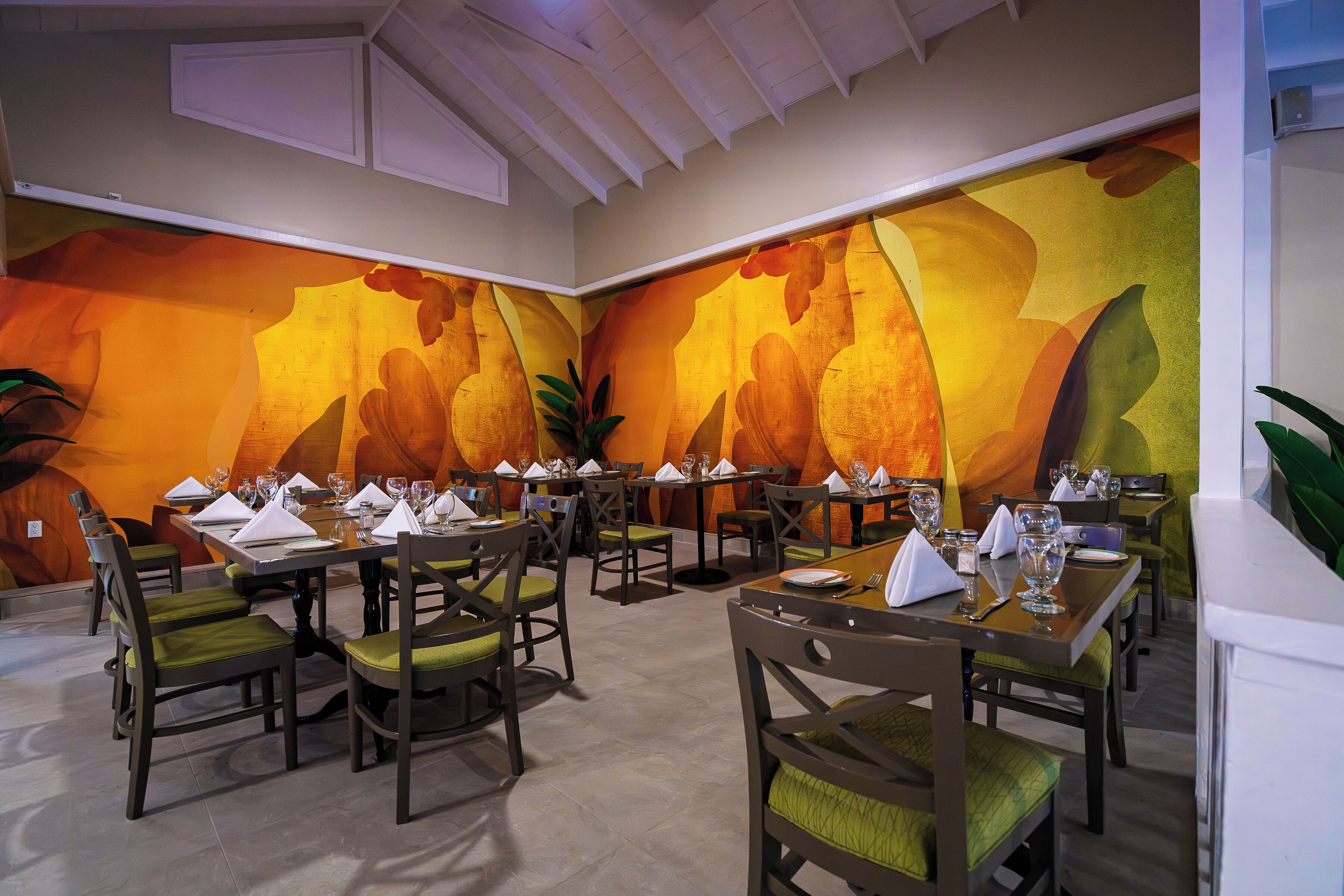 A restaurant with multiple tables and chairs, a high ceiling, and a large mural on the wall.