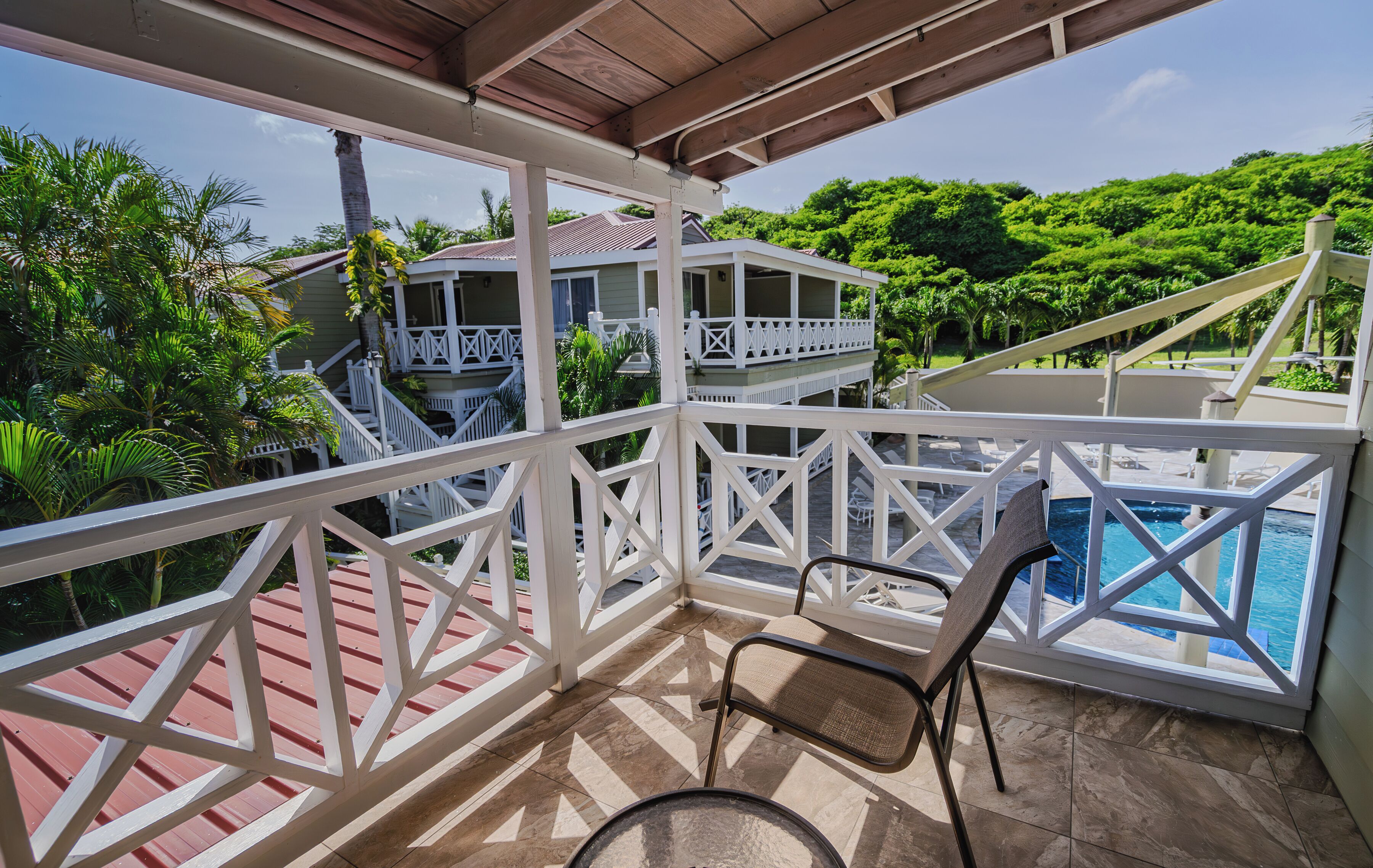 A covered balcony with a view of a pool and lush greenery.