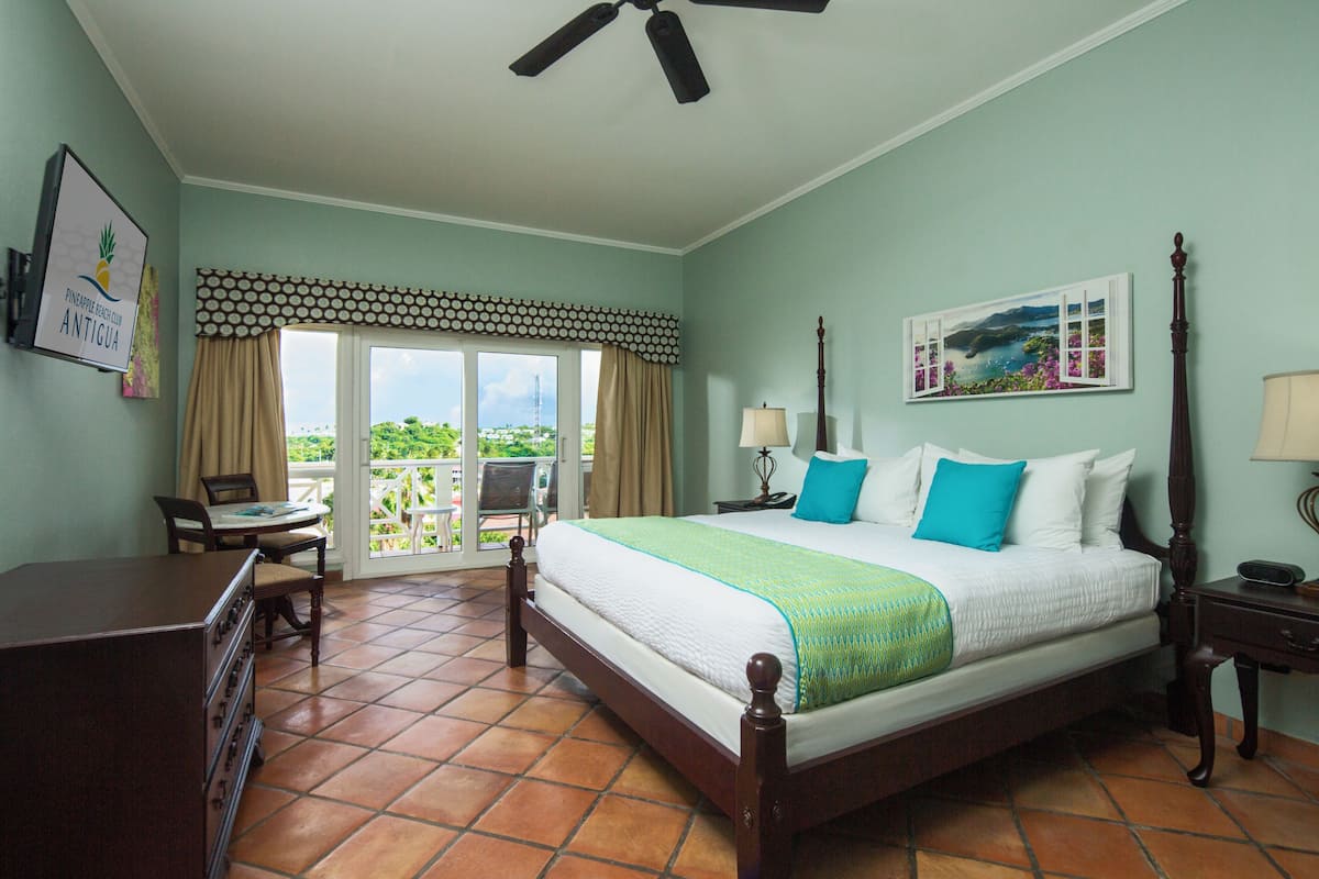 A bedroom with a bed, a desk, a chair, a dresser, a window with curtains, a ceiling fan, and a painting on the wall.
