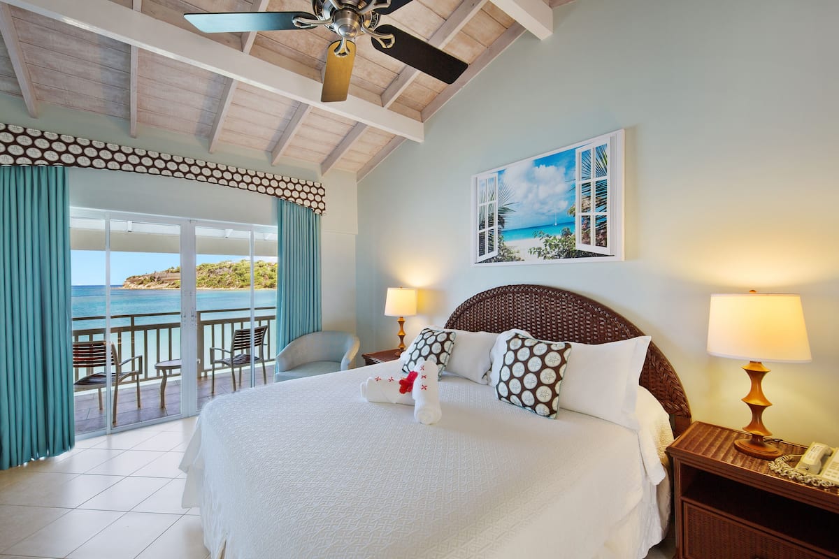A hotel room with a large bed, a balcony with a view of the sea, and a painting of a tropical scene.