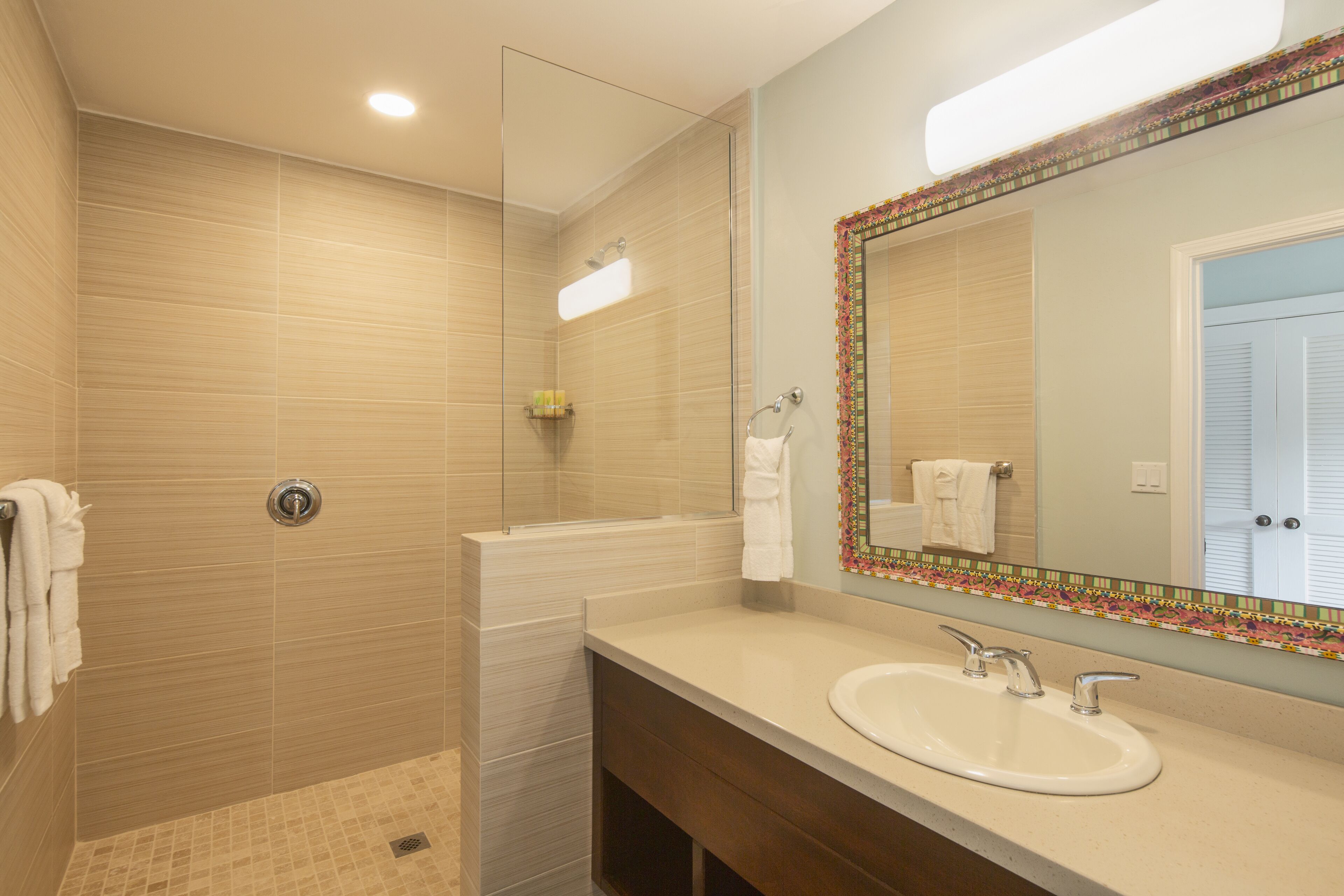 A modern bathroom with a glass-enclosed shower, a large mirror with a decorative frame, and a vanity with a sink and towel rack.