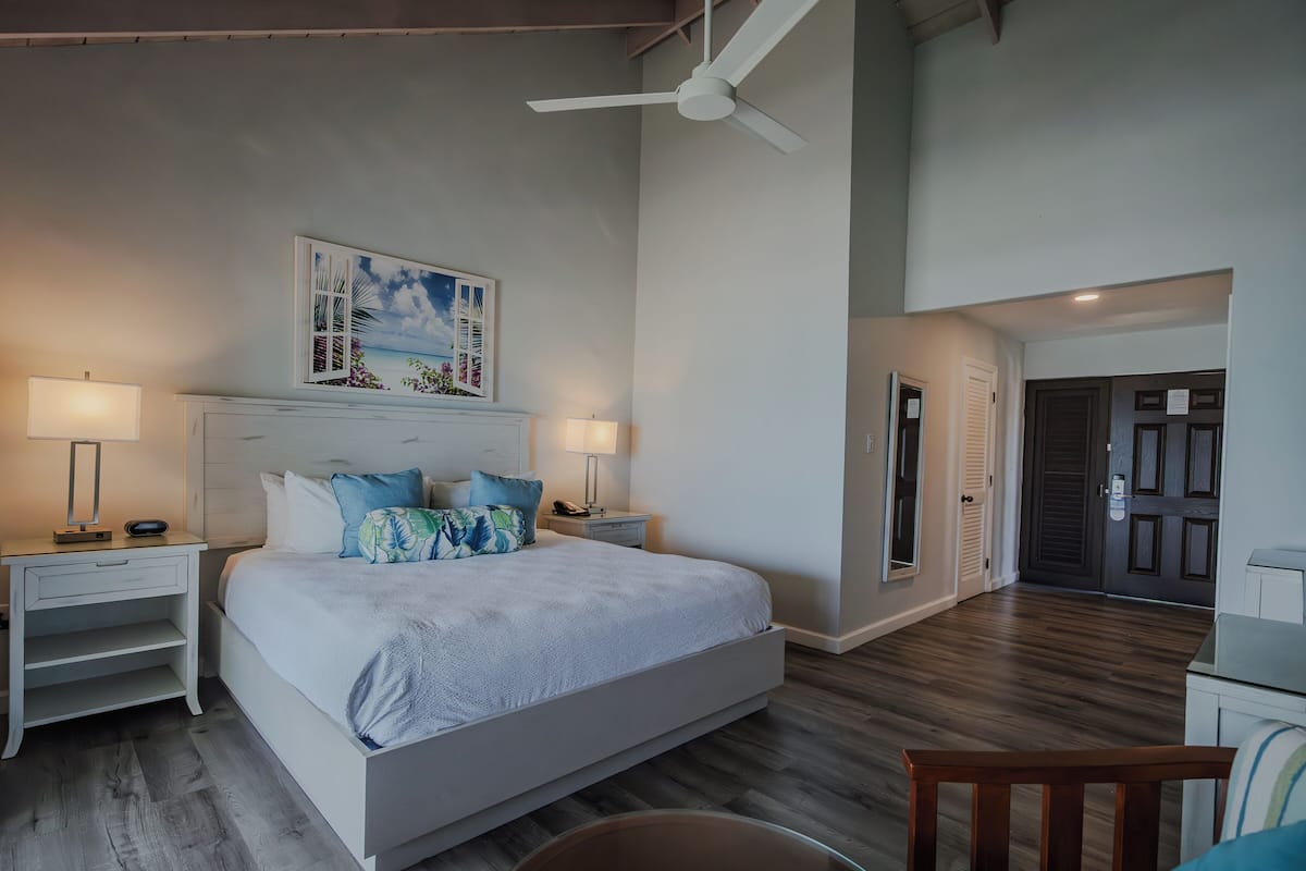 A bedroom with a bed, nightstands, a ceiling fan, a painting, and a wooden floor.