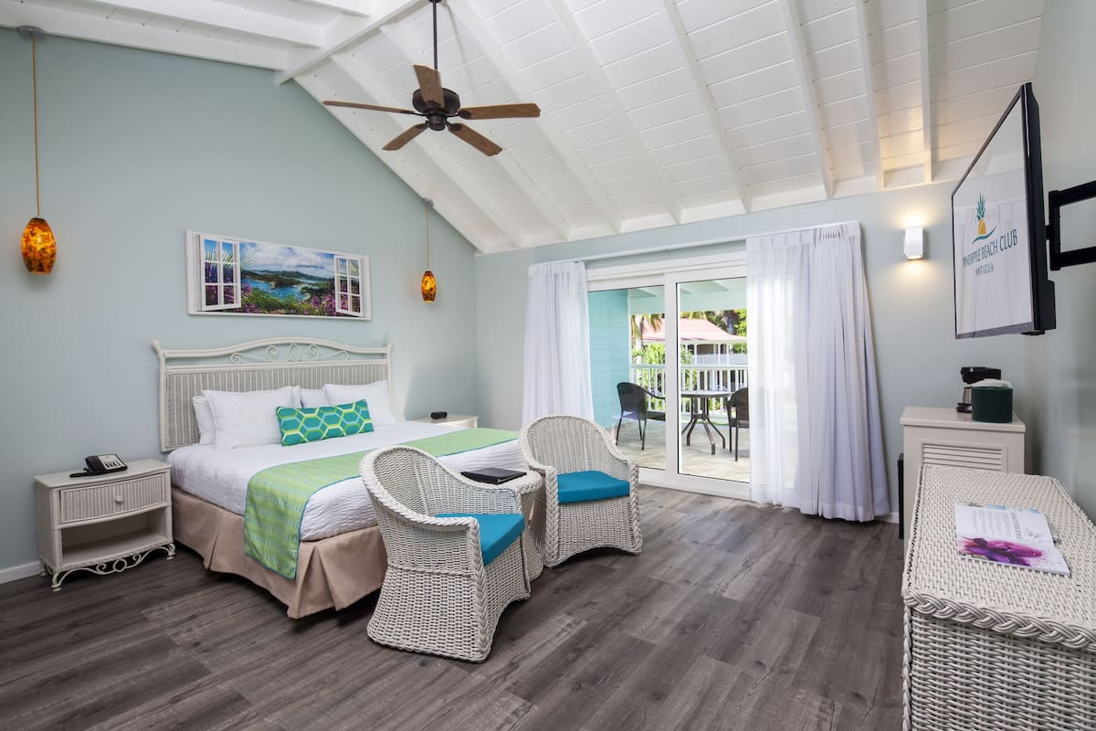 A bedroom with a bed, two wicker chairs, a nightstand, and a desk.