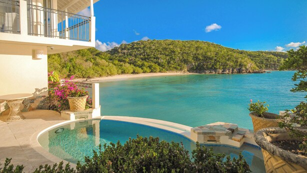 A pool with a clear view of the sea and a mountainous landscape in the background. - Blue Waters Resort & Spa (St. John's)