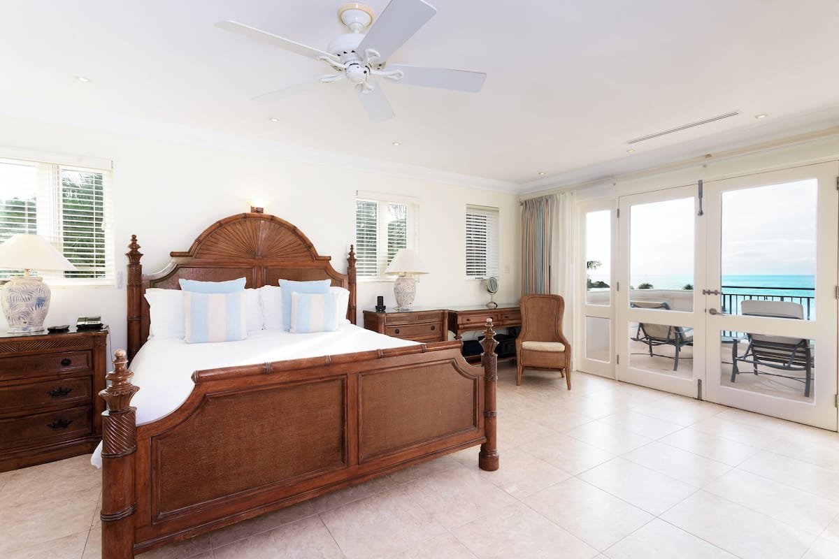 A spacious bedroom with a large bed, a ceiling fan, and a view of the ocean through the sliding glass doors.