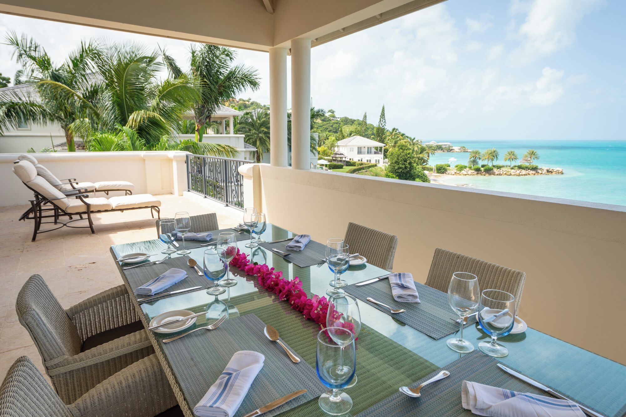 A dining table set for four with a view of the ocean and palm trees.