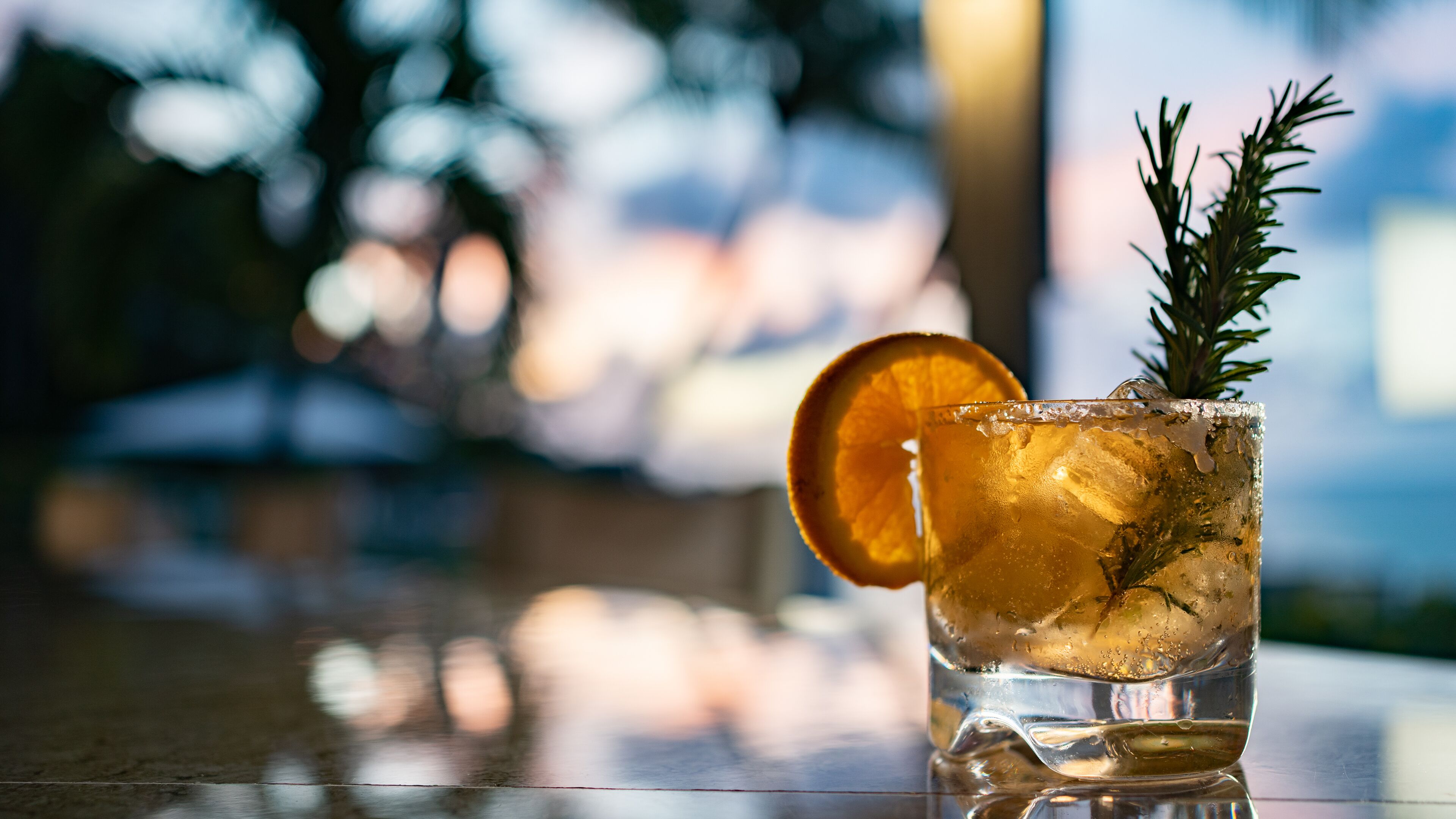 Un verre rempli de glaçons, une tranche d’orange et une branche de romarin.