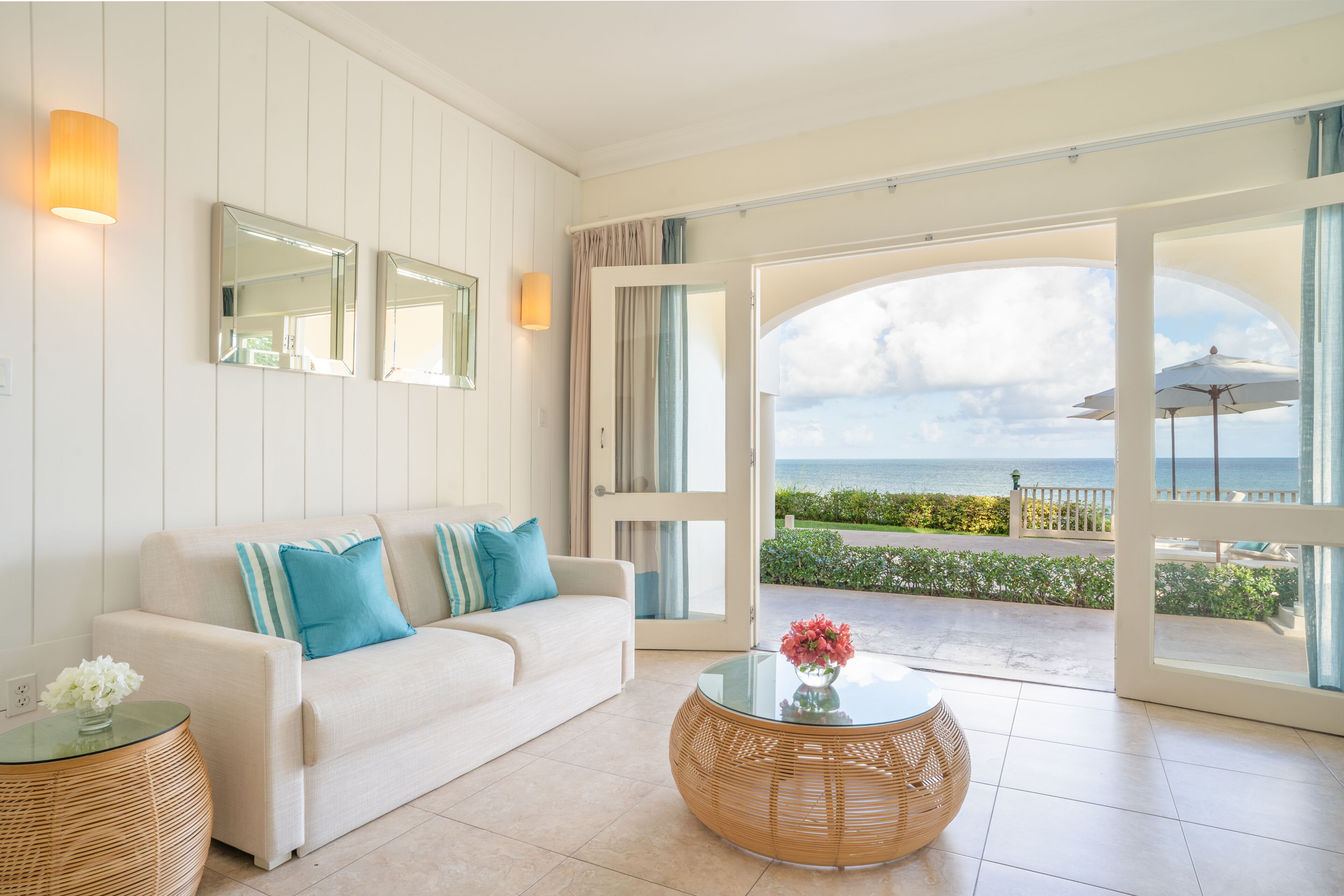 Un salon moderne avec un canapé blanc, une table basse en verre et une vue sur la mer grâce à de grandes fenêtres.