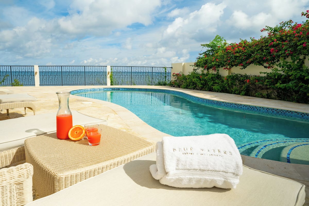 A poolside area with wicker lounge chairs, a bottle of orange juice, and a towel labeled "REFRESH".