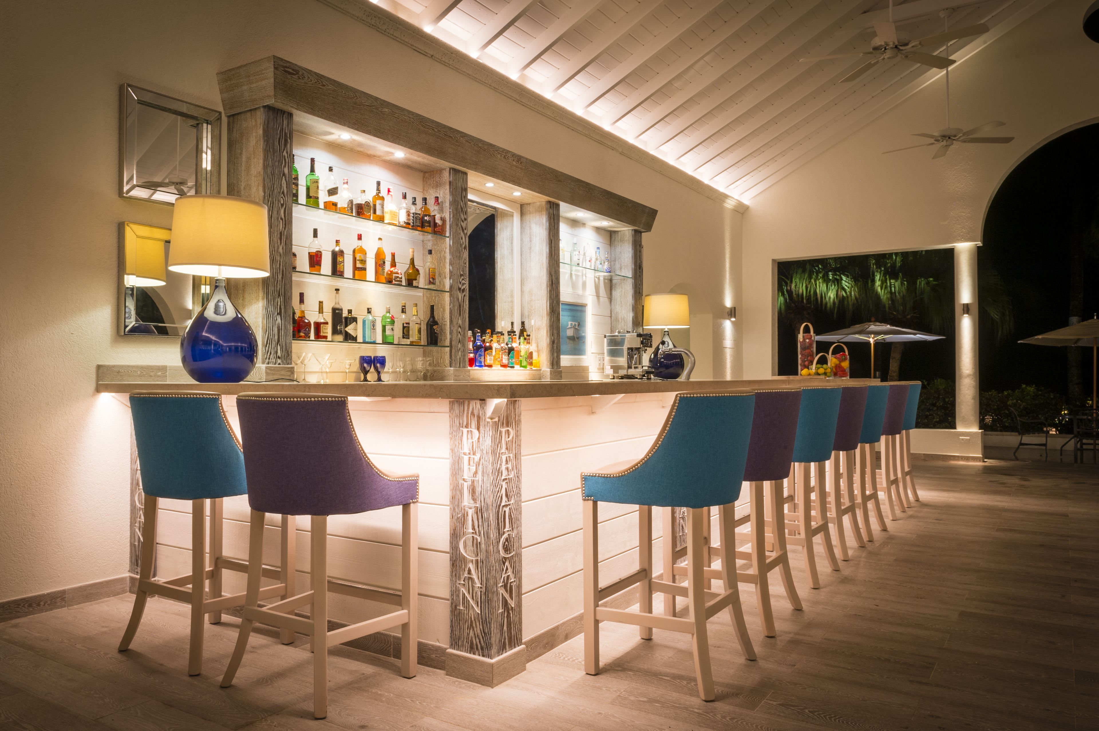 A bar area with a long counter, multiple bar stools, and a variety of bottles on shelves.