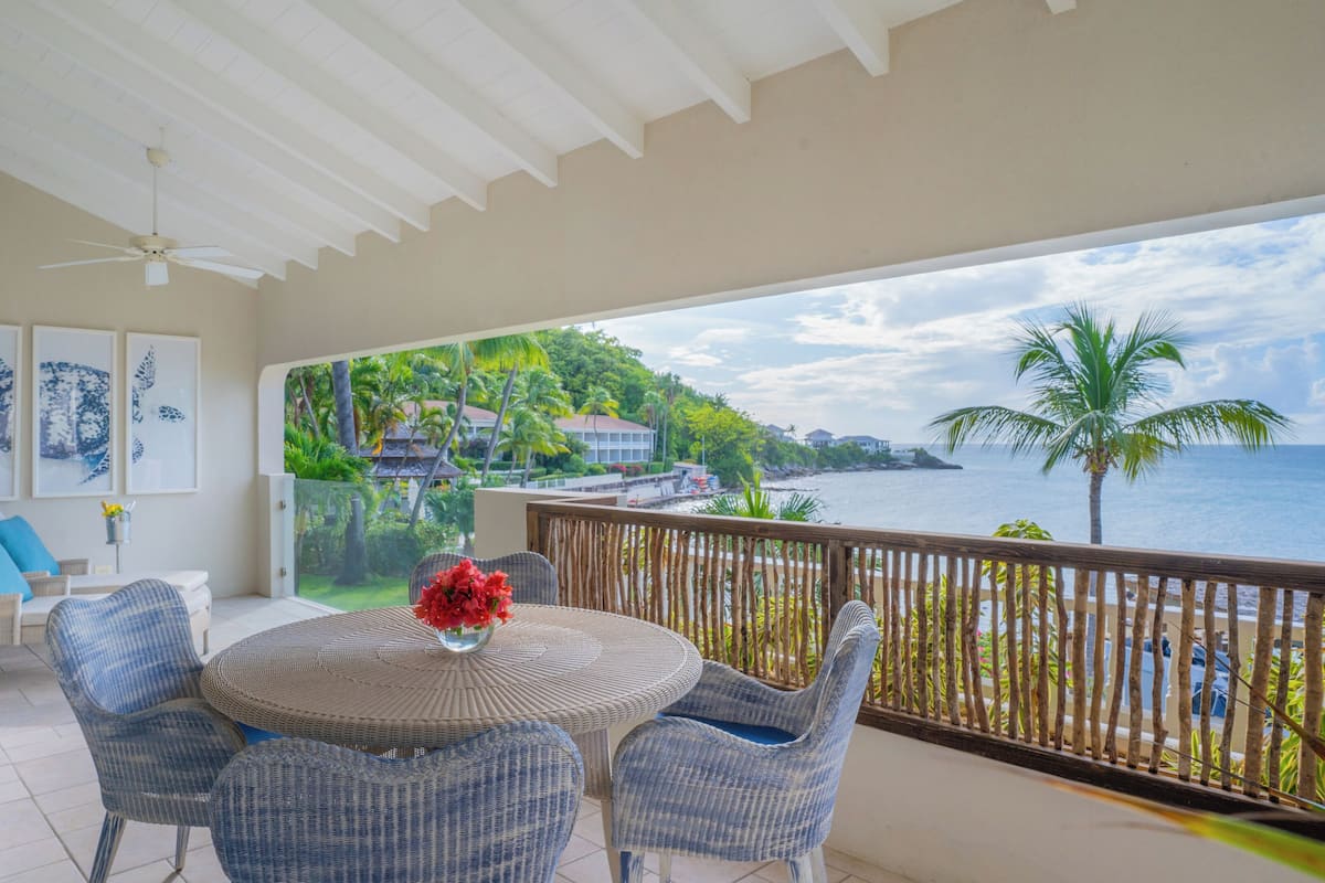 A balcony with wicker furniture, a view of the sea, and tropical vegetation.