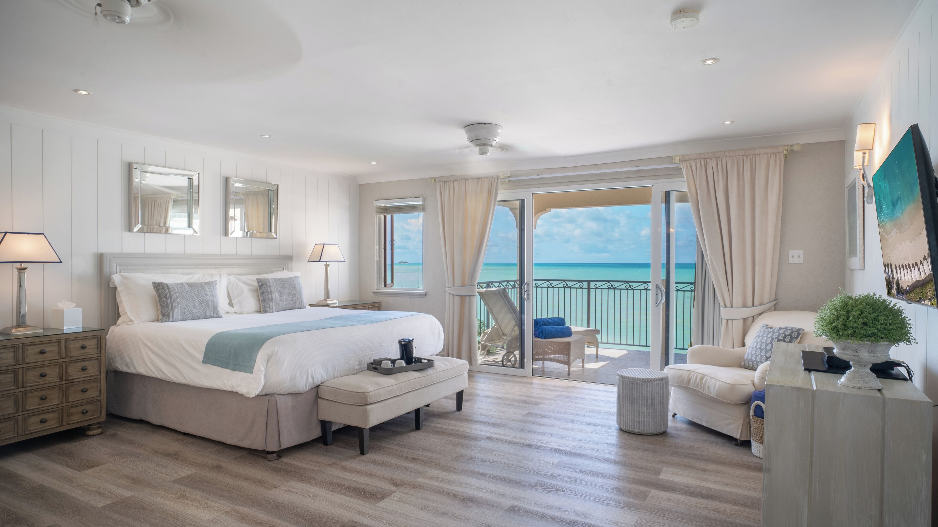 A spacious bedroom with a large bed, a balcony with a view of the sea, and a seating area with a view.