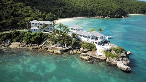 A coastal property with multiple buildings, a beach, and clear turquoise waters. - Blue Waters Resort & Spa (St. John's)