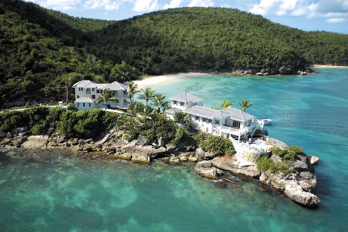 A coastal property with multiple buildings, a beach, and clear turquoise waters.