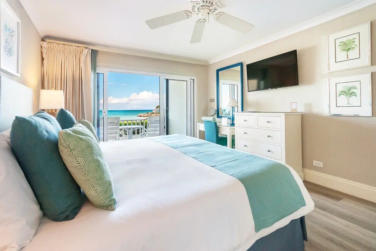 A hotel room with a bed, a TV, a desk, and a view of the ocean.