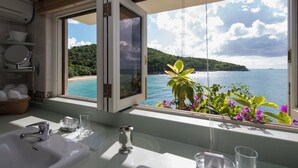 A bathroom with a large window offering a view of a beach and sea. - Blue Waters Resort & Spa (St. John's)