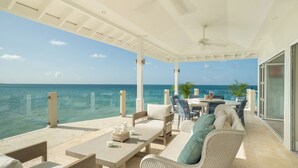 A covered outdoor seating area with a view of the ocean, featuring a table, chairs, and a ceiling fan. - Blue Waters Resort & Spa (St. John's)