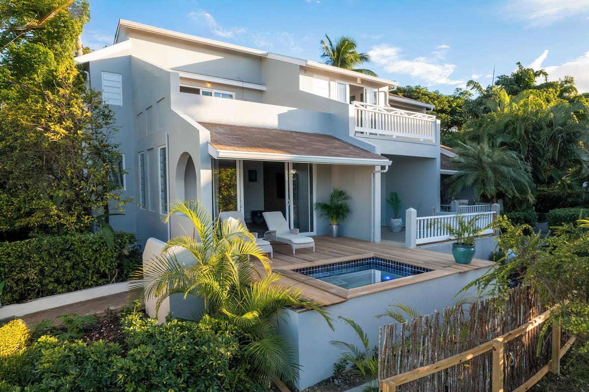 A two-story house with a swimming pool, outdoor seating, and lush greenery.
