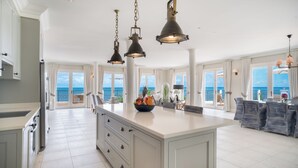 A spacious kitchen with a large island, pendant lighting, and a view of the ocean. - Blue Waters Resort & Spa (St. John's)