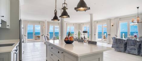 Una cocina amplia con una isla grande, iluminación colgante y vistas al océano.