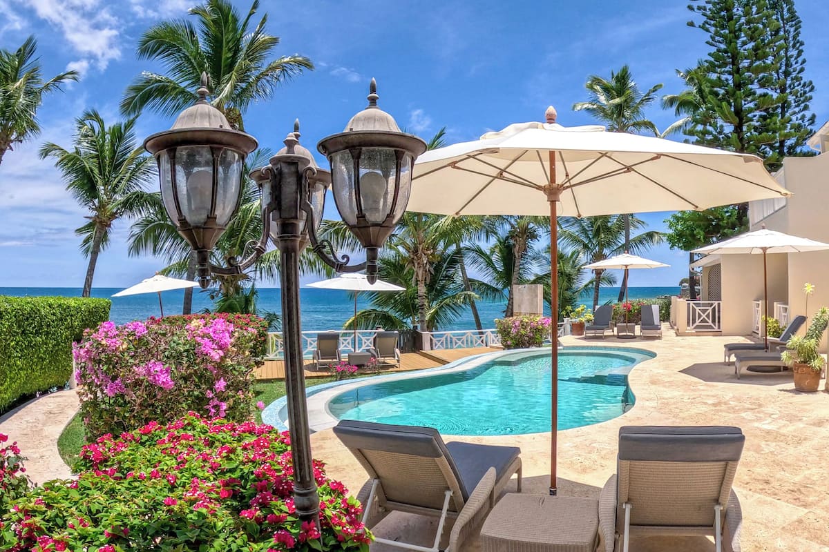 A pool area with lounge chairs, umbrellas, and a view of the ocean.
