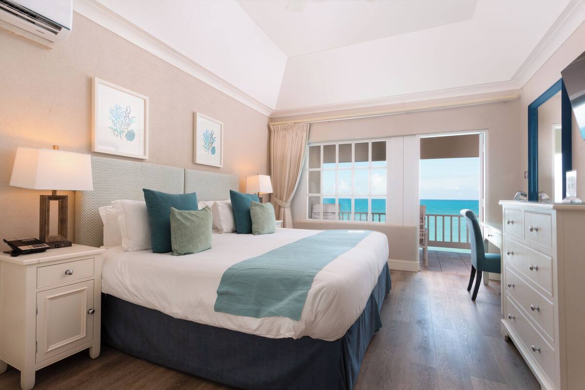 A bedroom with a large bed, bedside tables, a desk, and a view of the ocean.