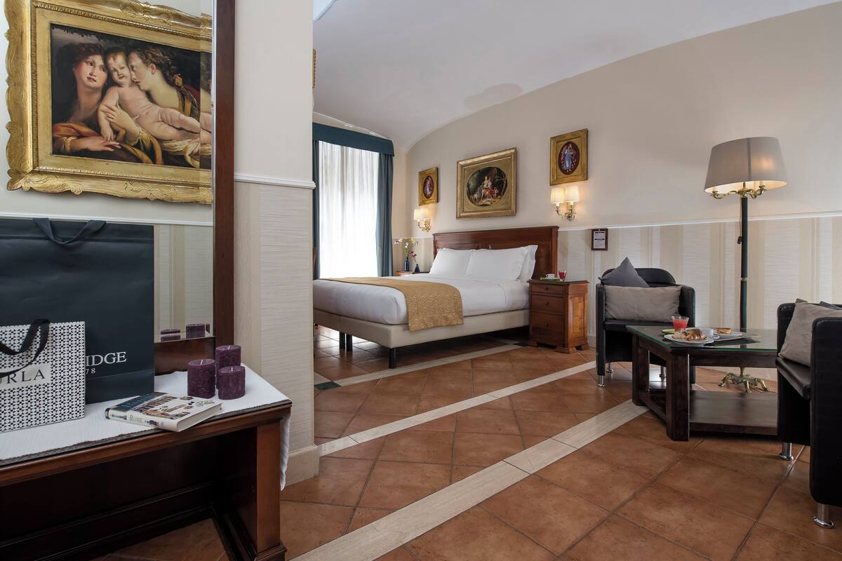 A hotel room with a bed, bedside table, lamp, and a painting on the wall.