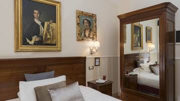 Habitación de hotel con una cama grande, cabecera de madera, mesita de noche, espejo y dos retratos enmarcados en la pared.