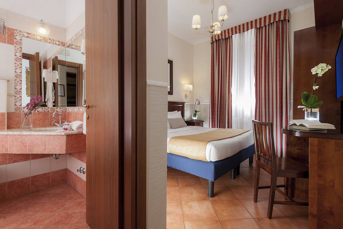 A hotel room with a bathroom, a bed, a desk, and a chair.