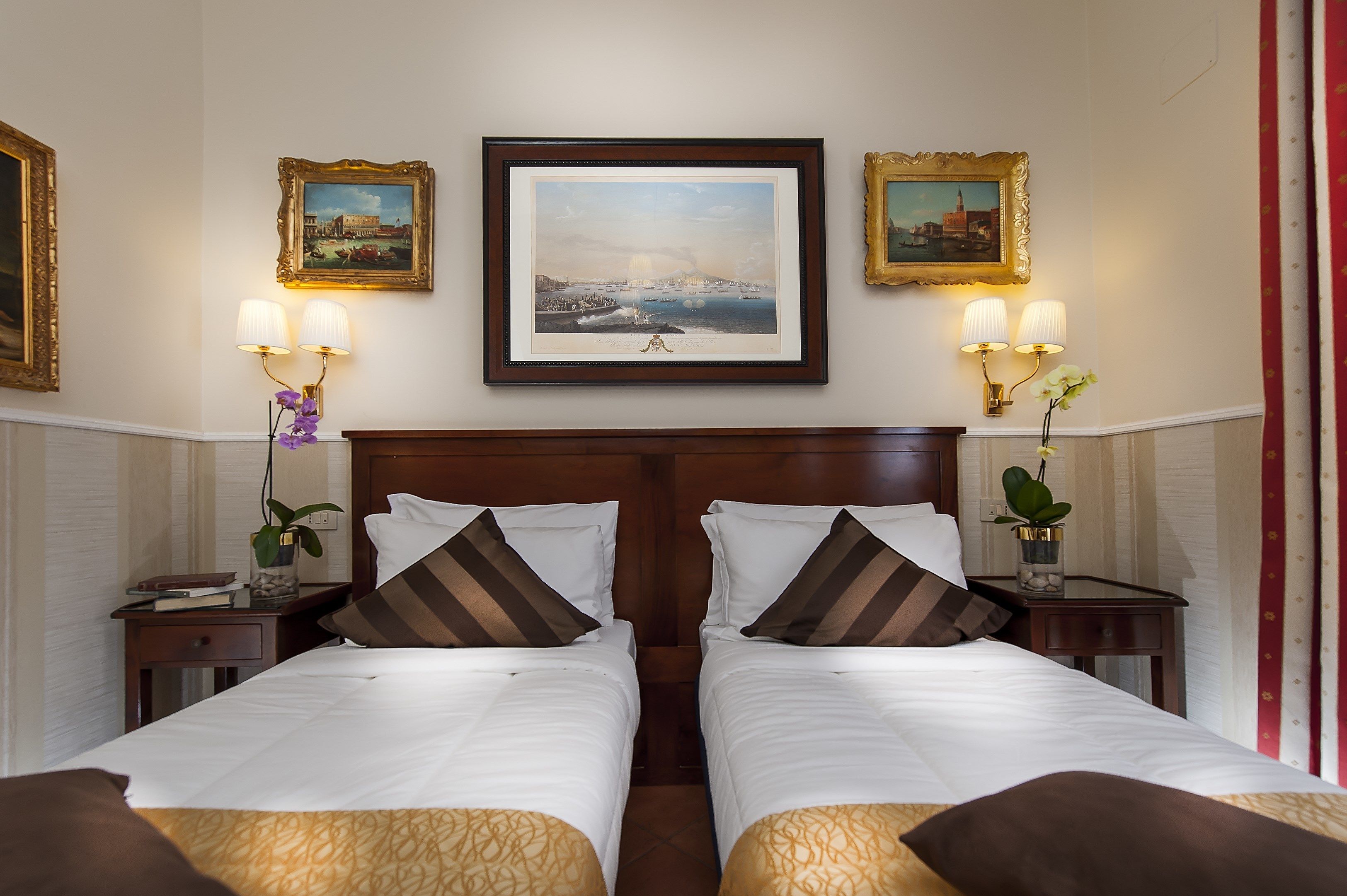 A hotel room with two beds, a large framed picture on the wall, and two bedside tables with lamps.