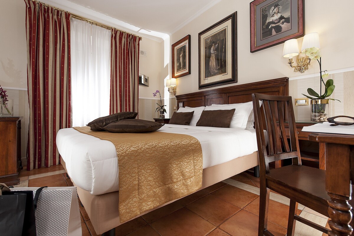 A hotel room with a large bed, a wooden headboard, a desk with a chair, and two wall-mounted lamps.