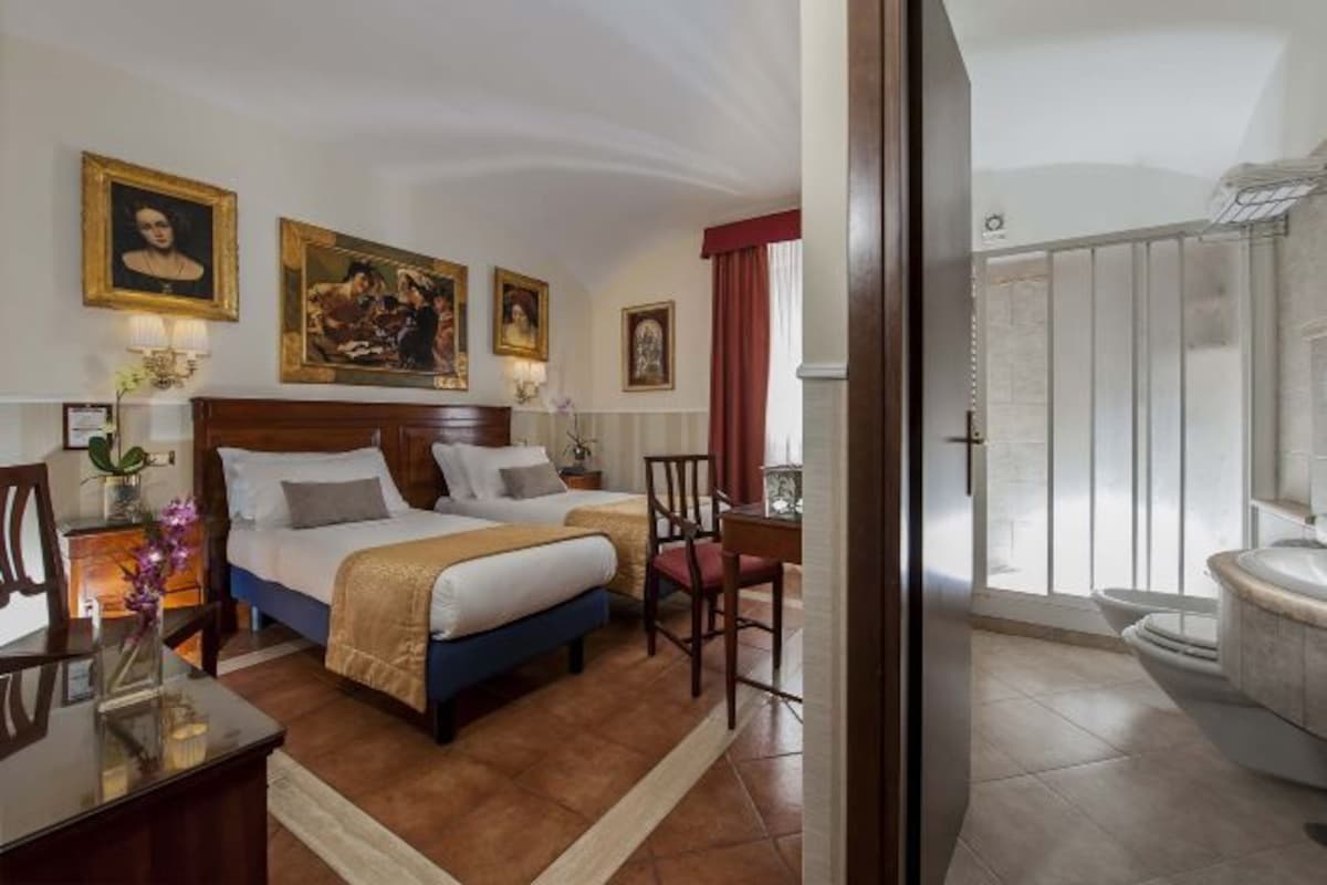 A hotel room with a double bed, a desk, a chair, and a bathroom with a shower and toilet.