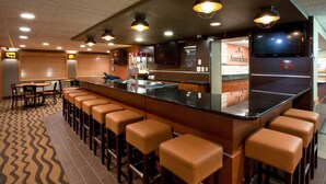A bar area with a long counter, multiple stools, and overhead lighting. - AmericInn by Wyndham Grafton (Grafton)