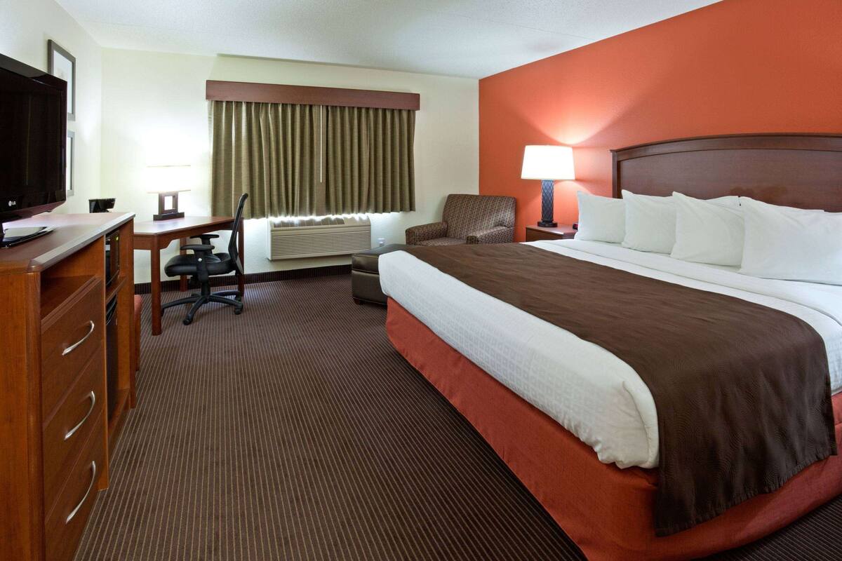 A hotel room with a large bed, a desk with a chair, a television, and a window with curtains.