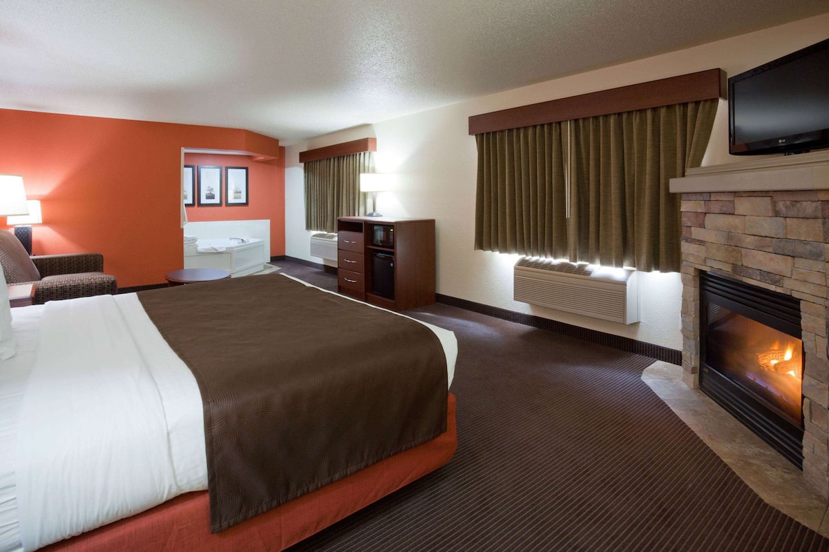 A hotel room with a large bed, a flat-screen TV, a fireplace, a desk, and a chair.