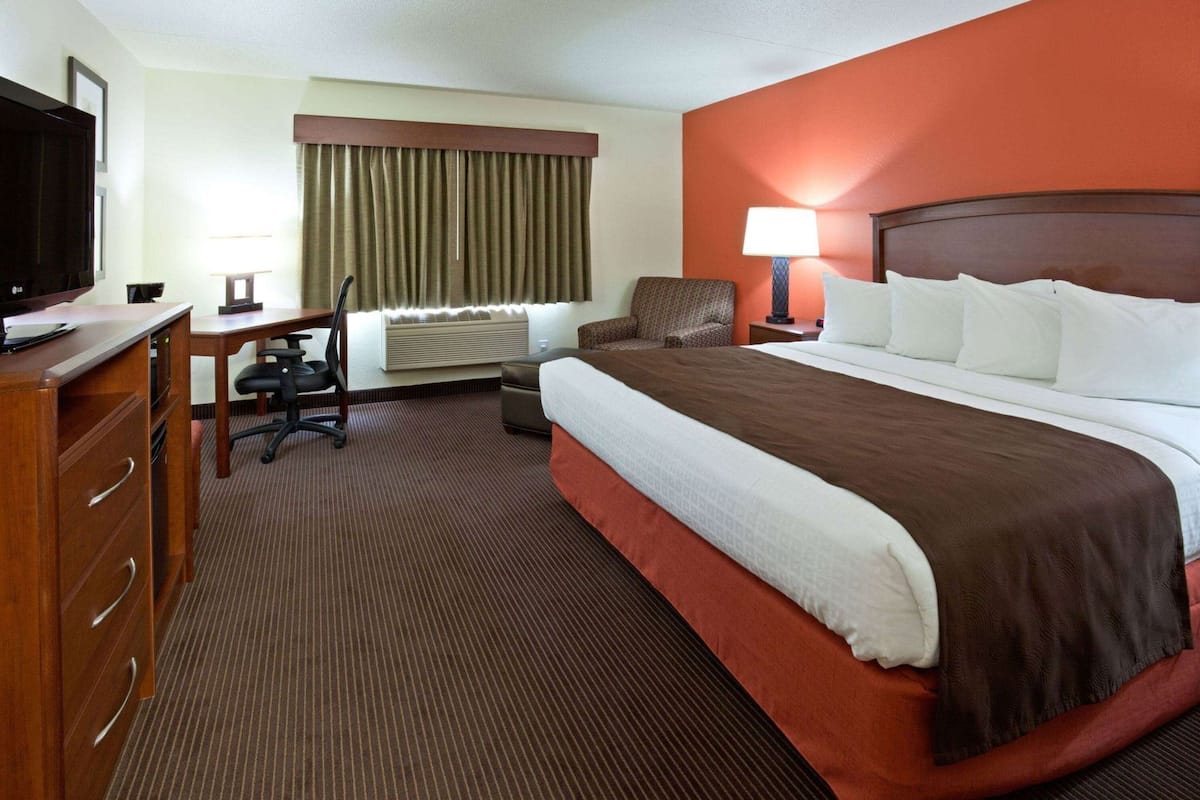 A hotel room with a bed, desk, chair, TV, and a lamp.