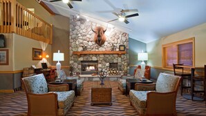 A cozy living room with a stone fireplace, comfortable seating, and a wooden staircase. - AmericInn by Wyndham Grafton (Grafton)