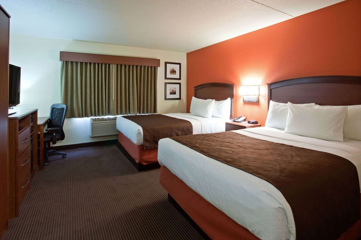A hotel room with two beds, a desk, a chair, a television, and a window with curtains.