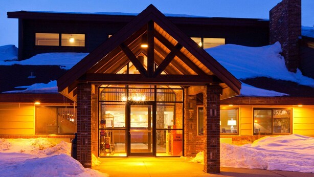 A hotel entrance with a wooden facade, large glass doors, and snow accumulation around the base. - AmericInn by Wyndham Grafton (Grafton)