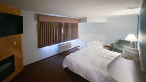 A hotel room with a large bed, a sitting area with a chair, a small table, a television, and a window with curtains. - Motel 6 Norway, MI (Norway)