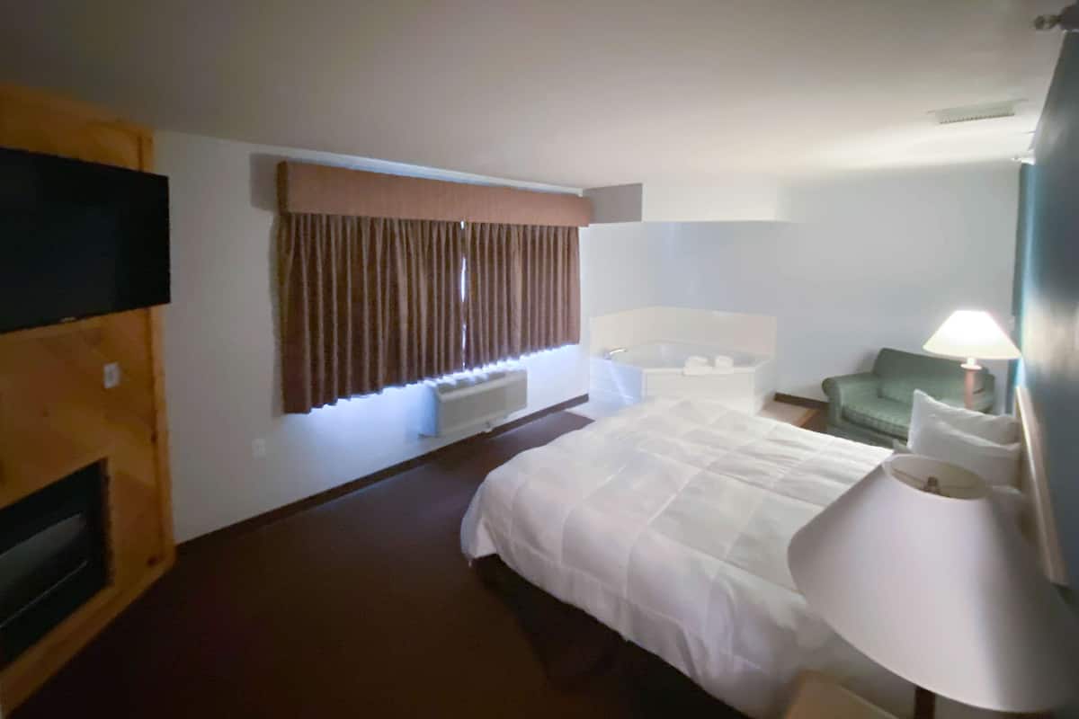 A hotel room with a large bed, a sitting area with a chair, a small table, a television, and a window with curtains.